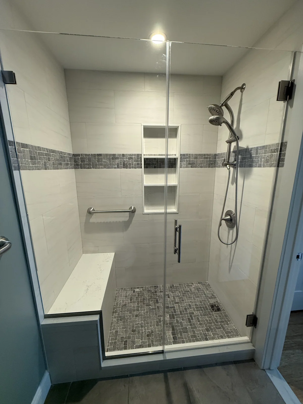 Glass-enclosed shower with a natural-stone feature band, custom niche, stone bench and stone curb.