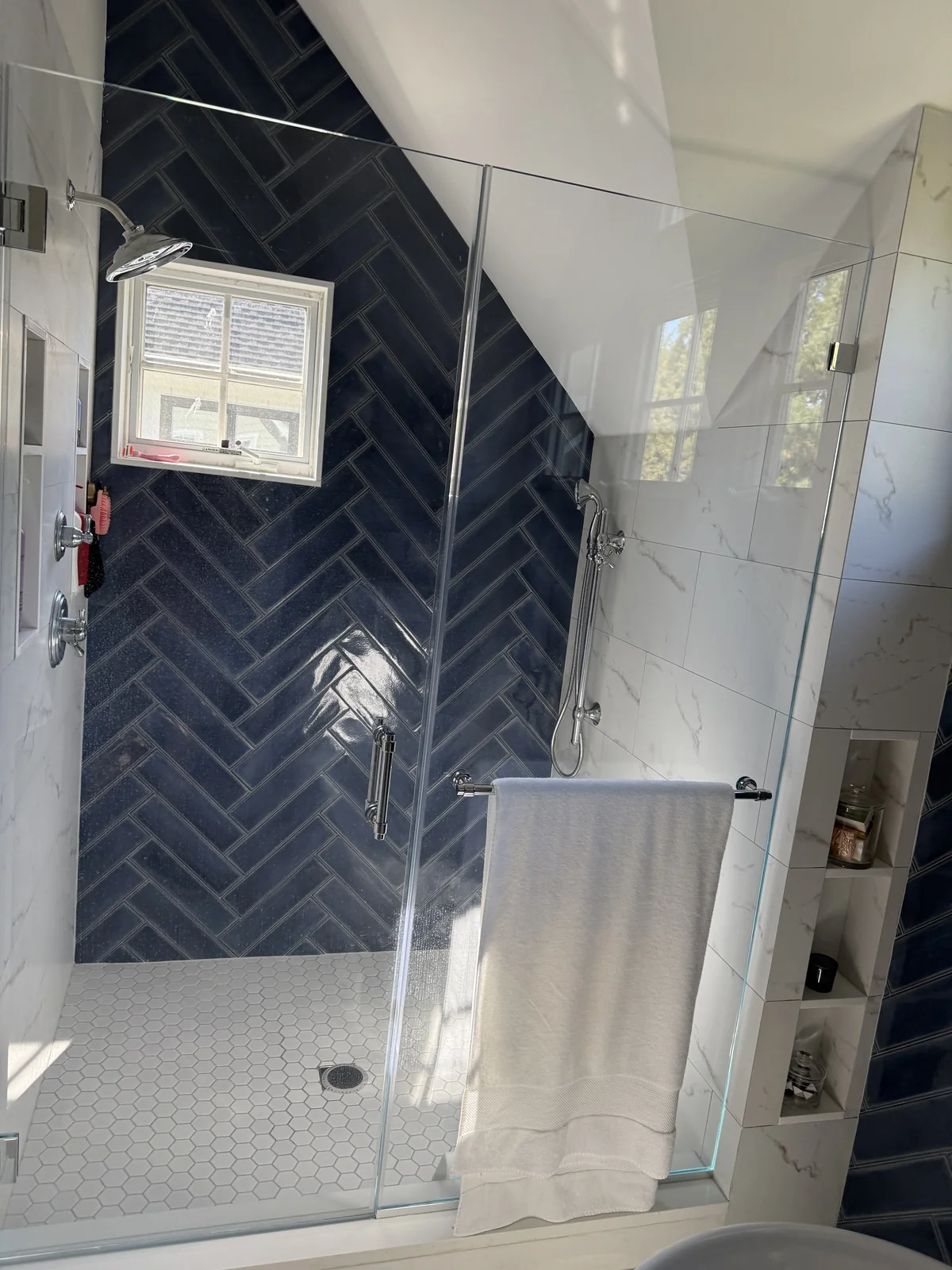 Shower with a dark-blue herringbone tile wall, light porcelain walls and a glass enclosure.
