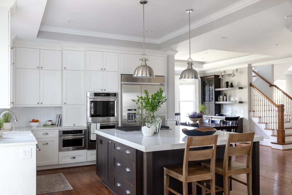 White kitchen with a dark island and a thick light stone countertop edge beside wooden stools.